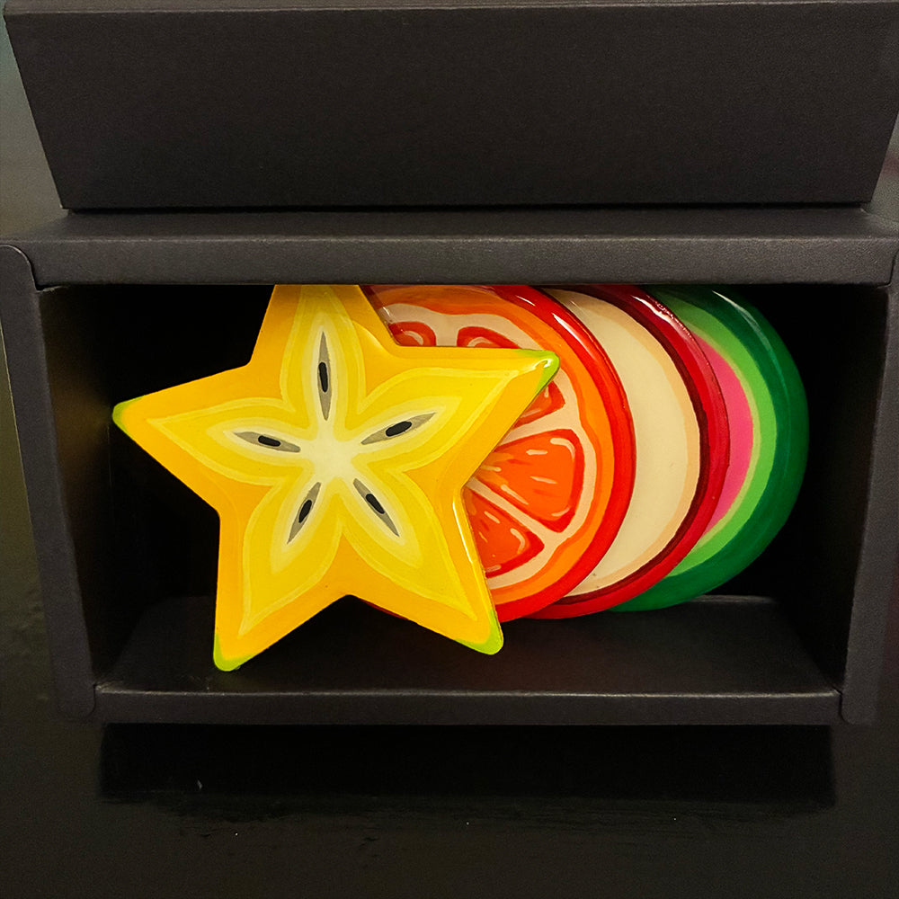 Colorful star-shaped and sliced fruit coasters in a black display box.