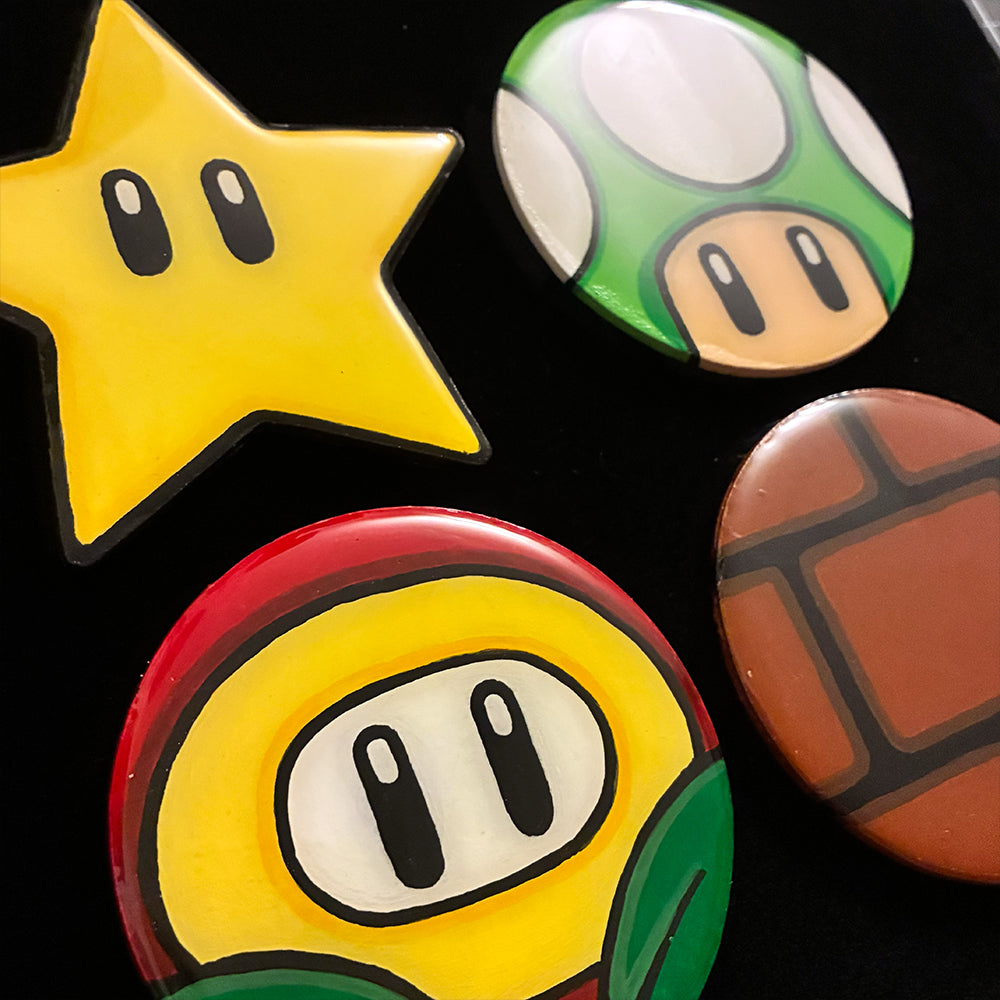 Four colorful coasters shaped like a star, mushroom, fire flower and brick power-ups on a black background