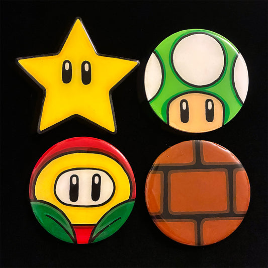 Four colorful coasters shaped like a star, mushroom, flower, and brick power-ups on a black background