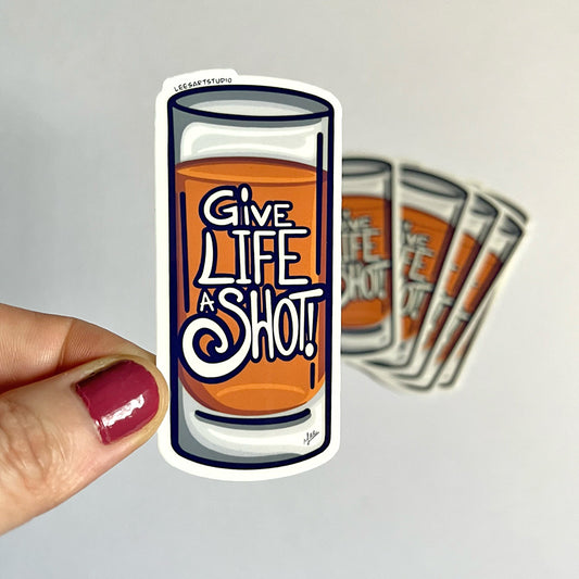 hand holding a Lees art studio give life a shot premium sticker